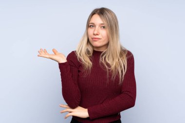 Bir şeyi anlamadığı için mutsuz olan soyutlanmış mavi arka planı olan genç sarışın kadın.