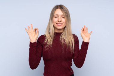 Zen pozisyonunda, soyutlanmış mavi arka planda genç sarışın kadın.