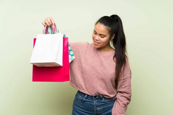 ショッピングバッグの多くを保持する孤立した緑の背景の上に若いティーンエイジャーアジアの女の子 — ストック写真