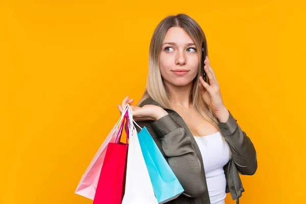 Young Blonde Woman Isolated Yellow Background Holding Shopping Bags Calling — 스톡 사진