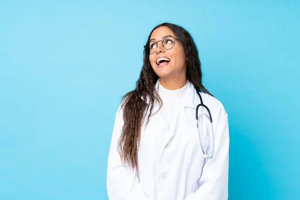 Junge Ärztin Über Isoliertem Blauem Hintergrund Lacht Und Blickt Auf — Stockfoto