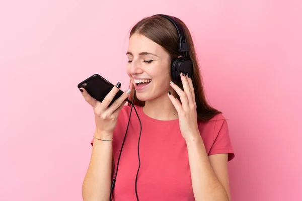 Mujer Joven Sobre Fondo Rosa Aislado Escuchando Música Con Móvil —  Fotos de Stock