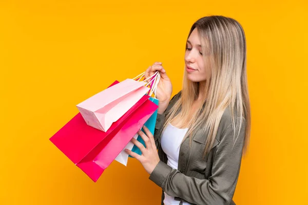 Young Blonde Woman Isolated Yellow Background Holding Shopping Bags — 스톡 사진