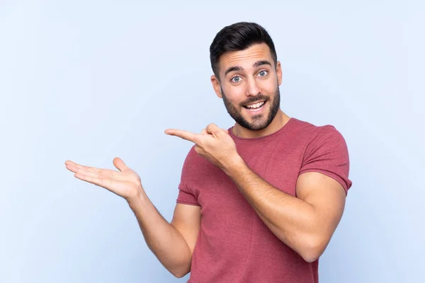 Joven Hombre Guapo Con Barba Sobre Fondo Azul Aislado Sosteniendo — Foto de Stock