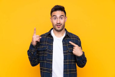 Sürpriz yüz ifadesi ile izole sarı arka plan üzerinde genç yakışıklı adam