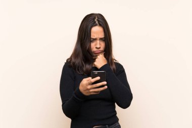 Beyaz kazaklı genç esmer kadın izole edilmiş arka planda düşünüyor ve bir mesaj gönderiyor.