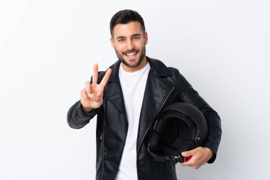 Motosiklet kasklı bir adam gülümsüyor ve zafer işareti gösteriyor.