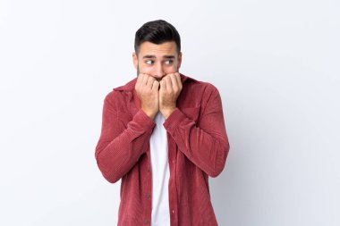 Sakallı, kadife ceket giyen genç yakışıklı adam izole edilmiş beyaz arka planda gergin ve elleri ağıza vermeye korkuyor.