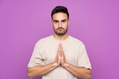 Mor arka planda kalan yakışıklı genç adam avuç içlerini bir arada tutuyor. İnsan bir şey ister.