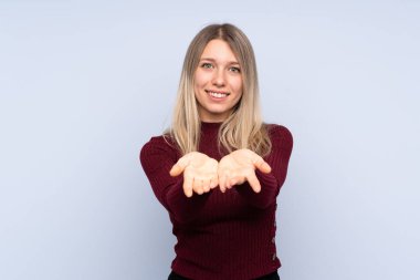 Bir reklam eklemek için avuç üzerinde copyspace hayali tutan izole mavi arka plan üzerinde Genç sarışın kadın