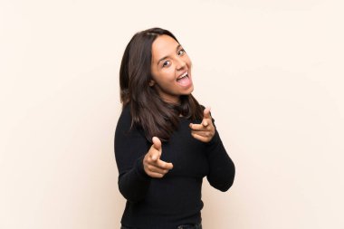 İzole edilmiş arka planda beyaz süveterli esmer bir kadın ön tarafı işaret ediyor ve gülümsüyor.