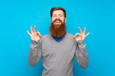 Kızıl saçlı, uzun sakallı, soyutlanmış mavi arka planlı, zen pozlu bir adam.