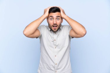 Sakallı, mavi arka planda, yüzünde sürpriz bir ifade olan yakışıklı bir genç.