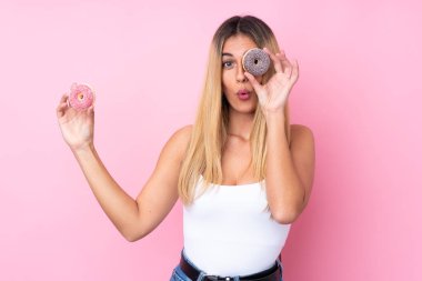 Genç Uruguaylı kadın pembe arka planda gözünün içinde donut tutuyor.