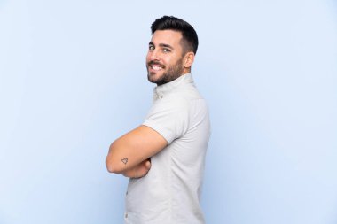 Sakallı, genç ve yakışıklı bir adam mavi arka planda gülüyor.