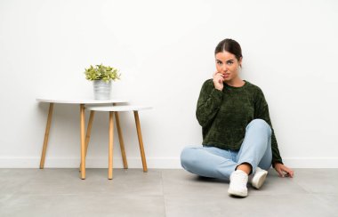 Yerde oturan genç kadın gergin ve korkmuş.