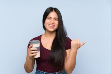 Genç Asyalı kız elinde kahve ile bir ürünü sunmak için kenarı işaret ediyor.