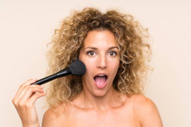 Makyaj fırçası ile kıvırcık saçlı genç sarışın kadın