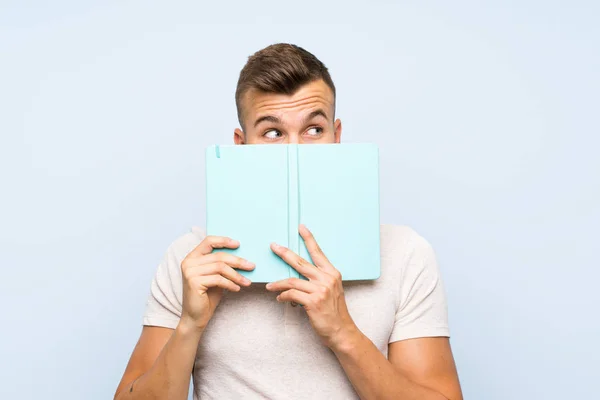 Joven Guapo Hombre Rubio Sobre Fondo Azul Aislado Sosteniendo Leyendo — Foto de Stock