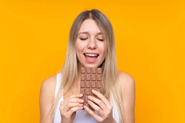 若いですブロンド女性以上隔離された青背景食べるチョコレートタブレット — ストック写真