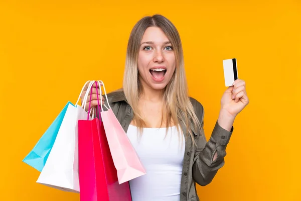 Young Blonde Woman Isolated Yellow Background Holding Shopping Bags Surprised — 스톡 사진