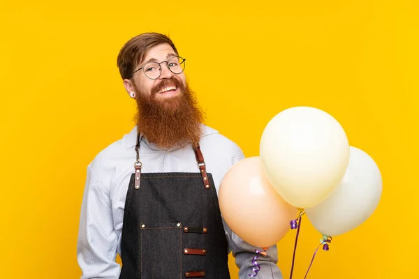 Holič s dlouhými vousy v zástěře drží balónky přes izolované žluté pozadí — Stock fotografie