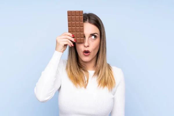 Mladá Blondýna Žena Přes Izolované Modré Pozadí Čokoládovou Tabletu Překvapený — Stock fotografie