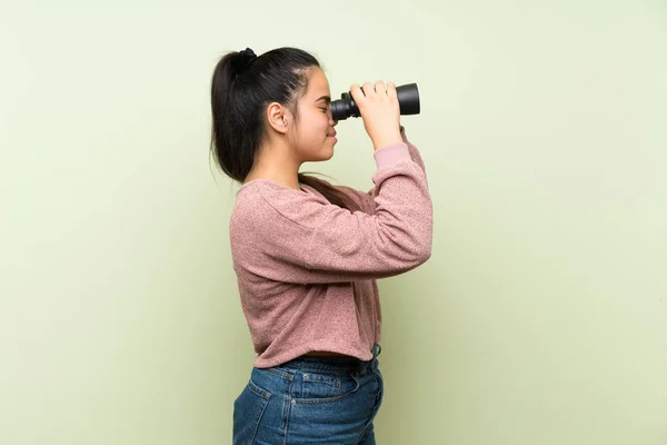 黒い双眼鏡で孤立した緑の背景の上に若いティーンエイジャーアジアの女の子 — ストック写真