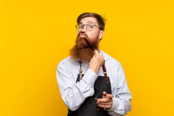 Peluquero con barba larga en delantal sobre fondo amarillo aislado — Foto de Stock