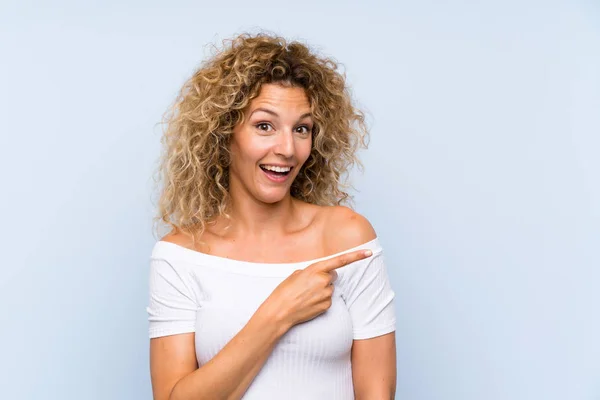 Jonge Blonde Vrouw Met Krullend Haar Geïsoleerde Blauwe Achtergrond Wijzende — Stockfoto