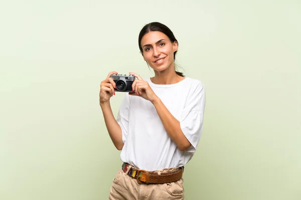 年轻女子在孤立的绿色背景拿着相机 — 图库照片