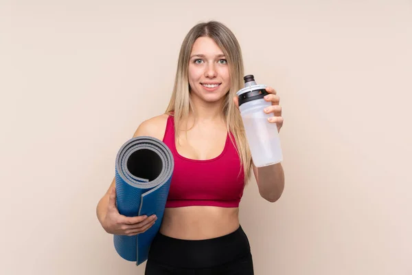 年轻的金发女运动员 背景偏僻 有运动水瓶和垫子 — 图库照片