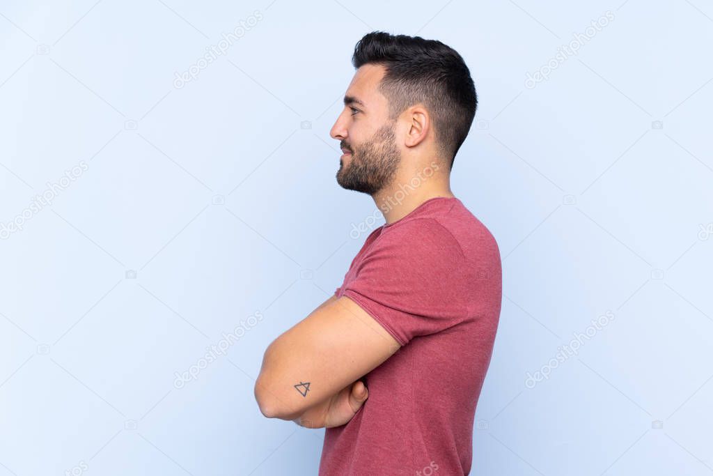Young handsome man with beard over isolated blue background in lateral position