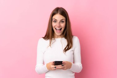 Soyutlanmış pembe arka planı olan genç bir kadın şaşırdı ve bir mesaj gönderiyor.