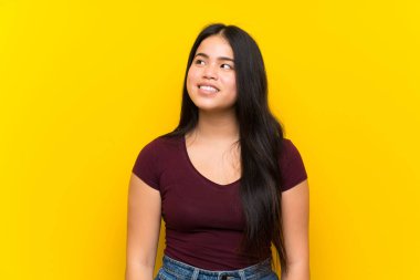 Genç Asyalı kız izole edilmiş sarı arka plan gülüyor ve yukarı bakıyor.