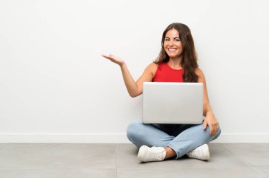 Avuç içinde hayali copyspace tutan katta oturan bir dizüstü bilgisayar ile genç kadın