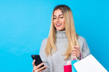 Genç Uruguaylı kadın mavi arka planda, elinde alışveriş torbalarıyla bir arkadaşına cep telefonuyla bir mesaj yazıyor.