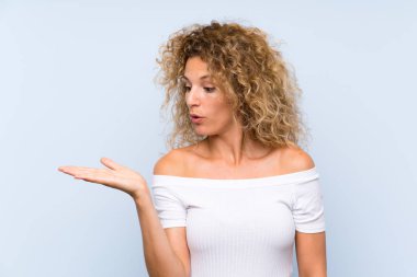 Sarışın, kıvırcık saçlı, izole edilmiş mavi arka planı olan genç bir kadın.