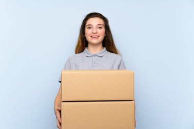 Genç esmer kız izole edilmiş mavi arka planda bir kutu tutuyor ve başka bir yere götürüyor.