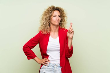 Parmakları geçiş ve en iyi dilek ile izole yeşil arka plan üzerinde kıvırcık saçlı genç sarışın kadın