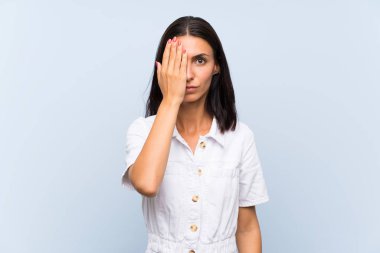 Elle bir göz kapsayan izole mavi arka plan üzerinde genç kadın