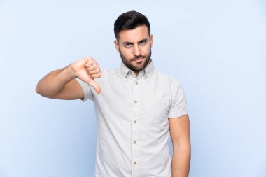 Sakallı, mavi arka planda genç ve yakışıklı bir adam baş parmağını aşağı gösteriyor.