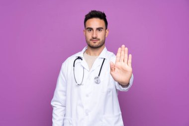 Genç adam doktor önlüğü giyiyor ve dur işareti yapıyor.