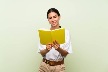Izole yeşil arka plan üzerinde genç kadın tutma ve bir kitap okuma