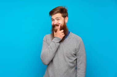 Kızıl saçlı, uzun sakallı, soyutlanmış mavi arka planda gülümseyen bir adam.