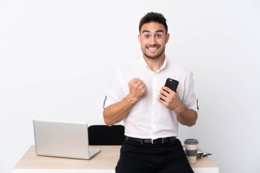 İş yerinde cep telefonlu genç bir işadamı zaferi kutluyor.
