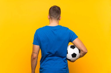Sarı arka planda futbol topu tutan yakışıklı sarışın genç adam.