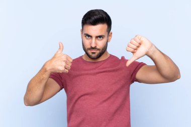 Mavi arka planda sakallı yakışıklı genç adam iyiye-kötüye işaret yapıyor. Evet ya da hayır arasında kararsız