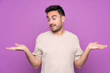 Mor arka plan üzerinde genç yakışıklı bir adam iki eliyle kopyalama alanını tutuyor.