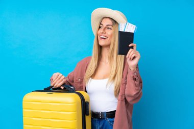 Genç Uruguaylı kadın izole edilmiş mavi arka planda, bavul ve pasaportla tatilde.